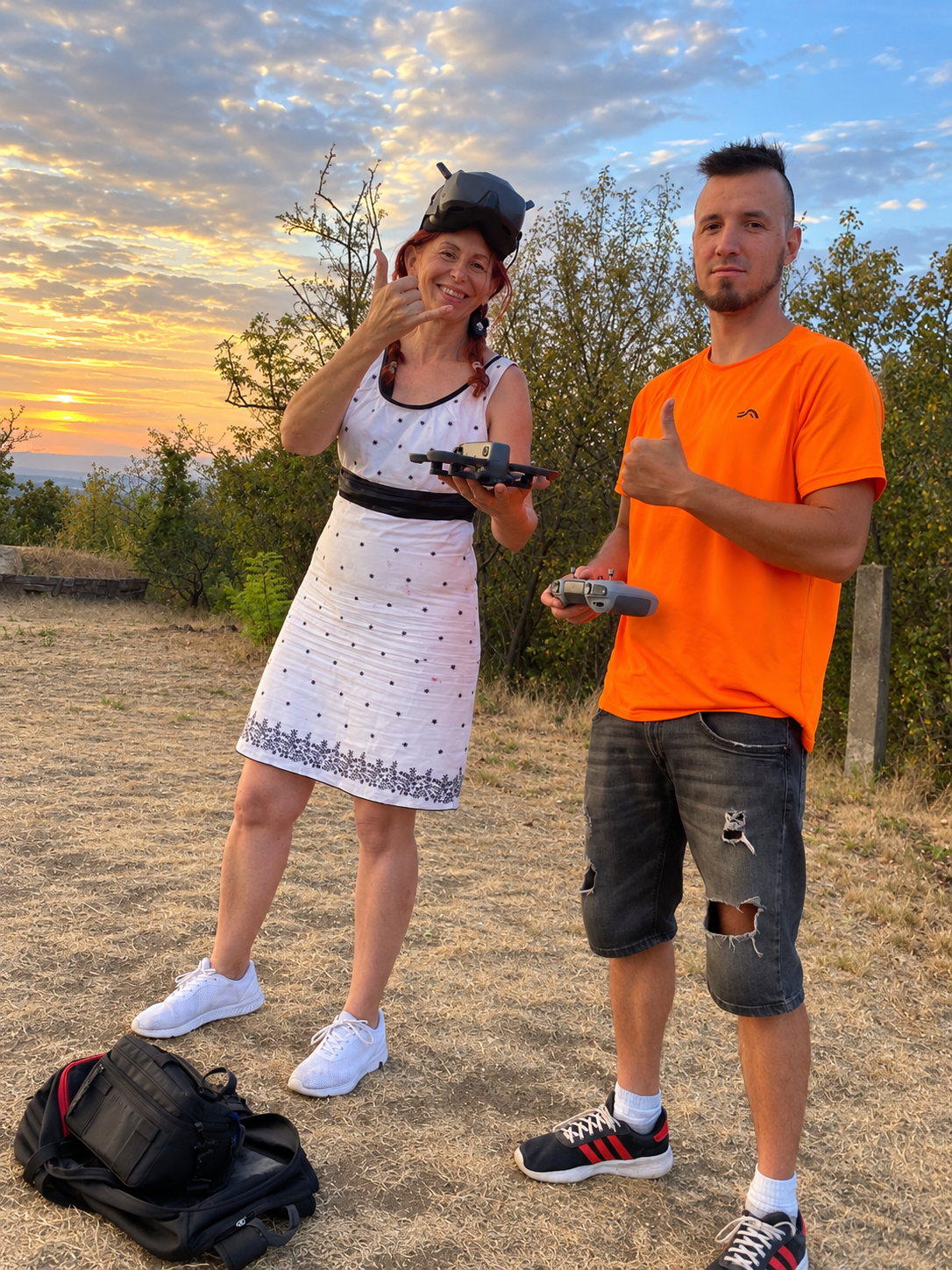 Tamás Megyeri and a guest holding FPV goggles, a controller and a drone at sunset